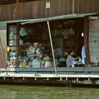 Asian woman working inside a cluttered store on a waterside urban setting.